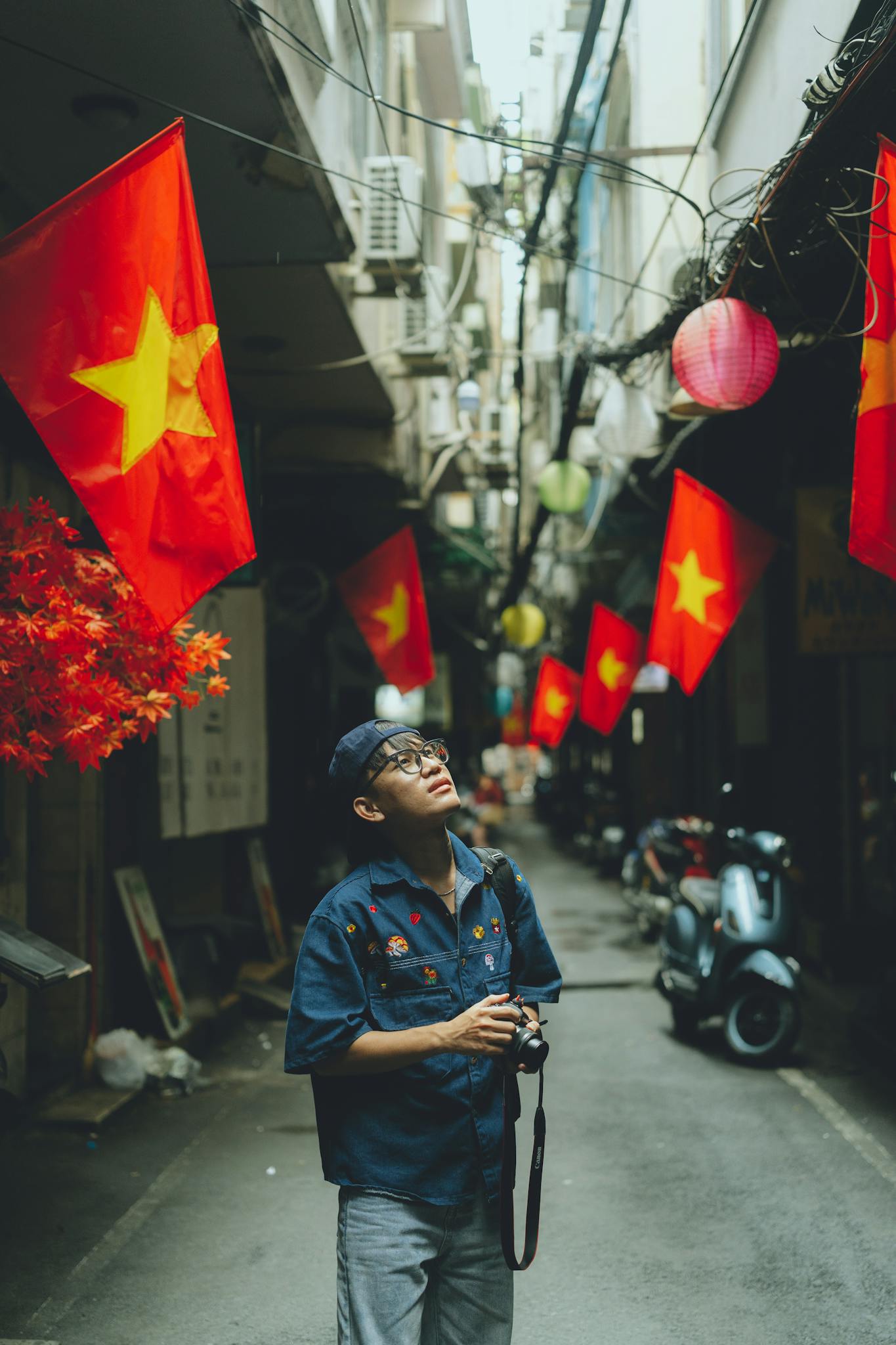 A man explores a narrow alley in Ho Chi Minh City adorned with Vietnamese flags.